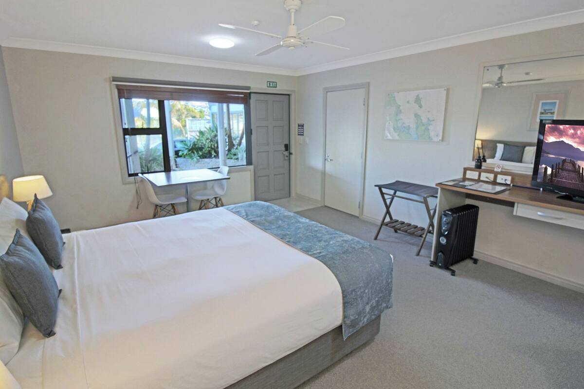 A hotel room with a bed, desk, chair, computer, and a TV.