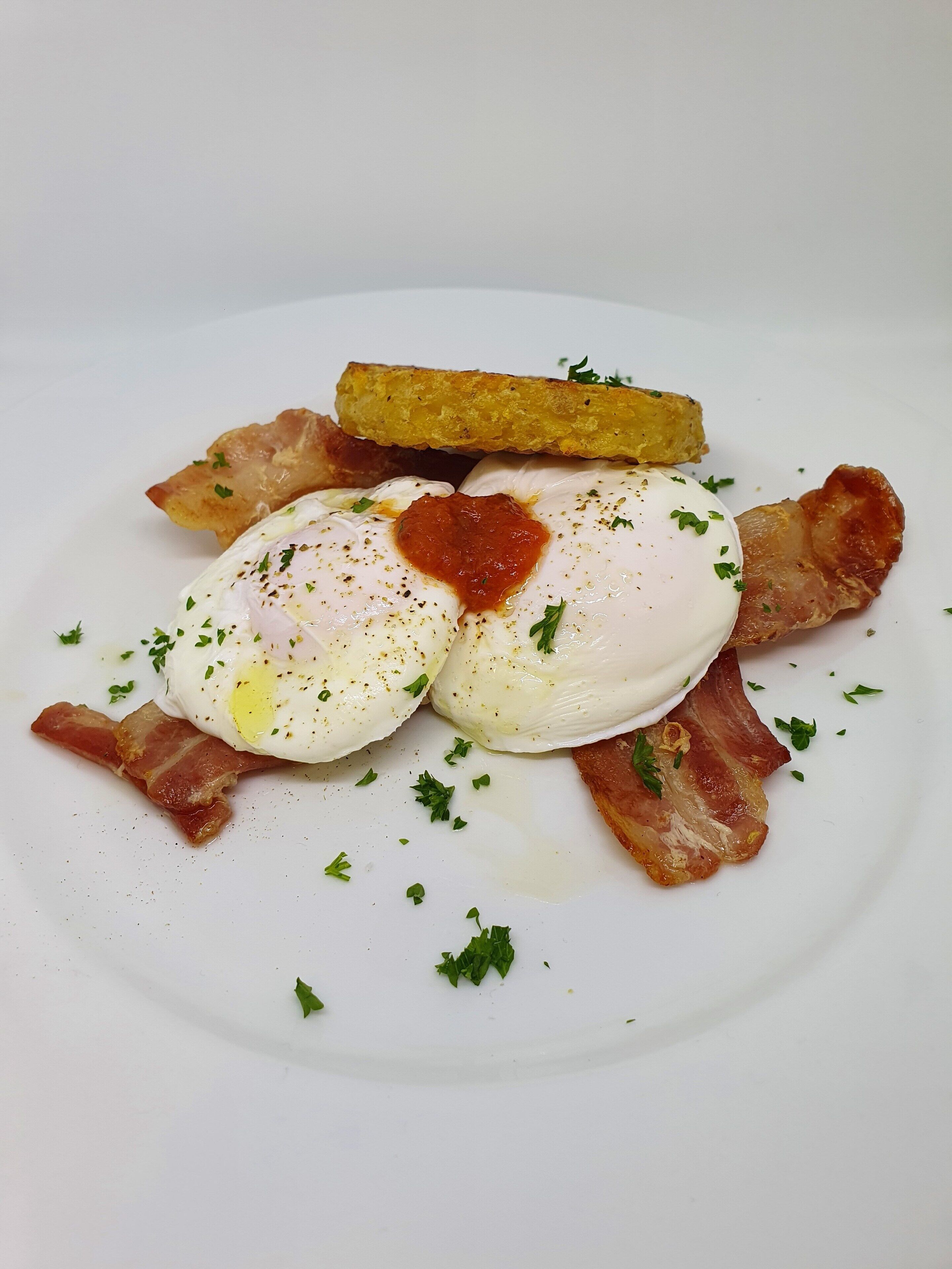 A plate with poached eggs, bacon, and a fried potato.