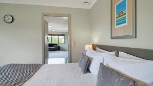 A bedroom with a large bed, a bedside table, a clock, and a framed picture on the wall. - Whangaparaoa Lodge Motel (Whangaparaoa)