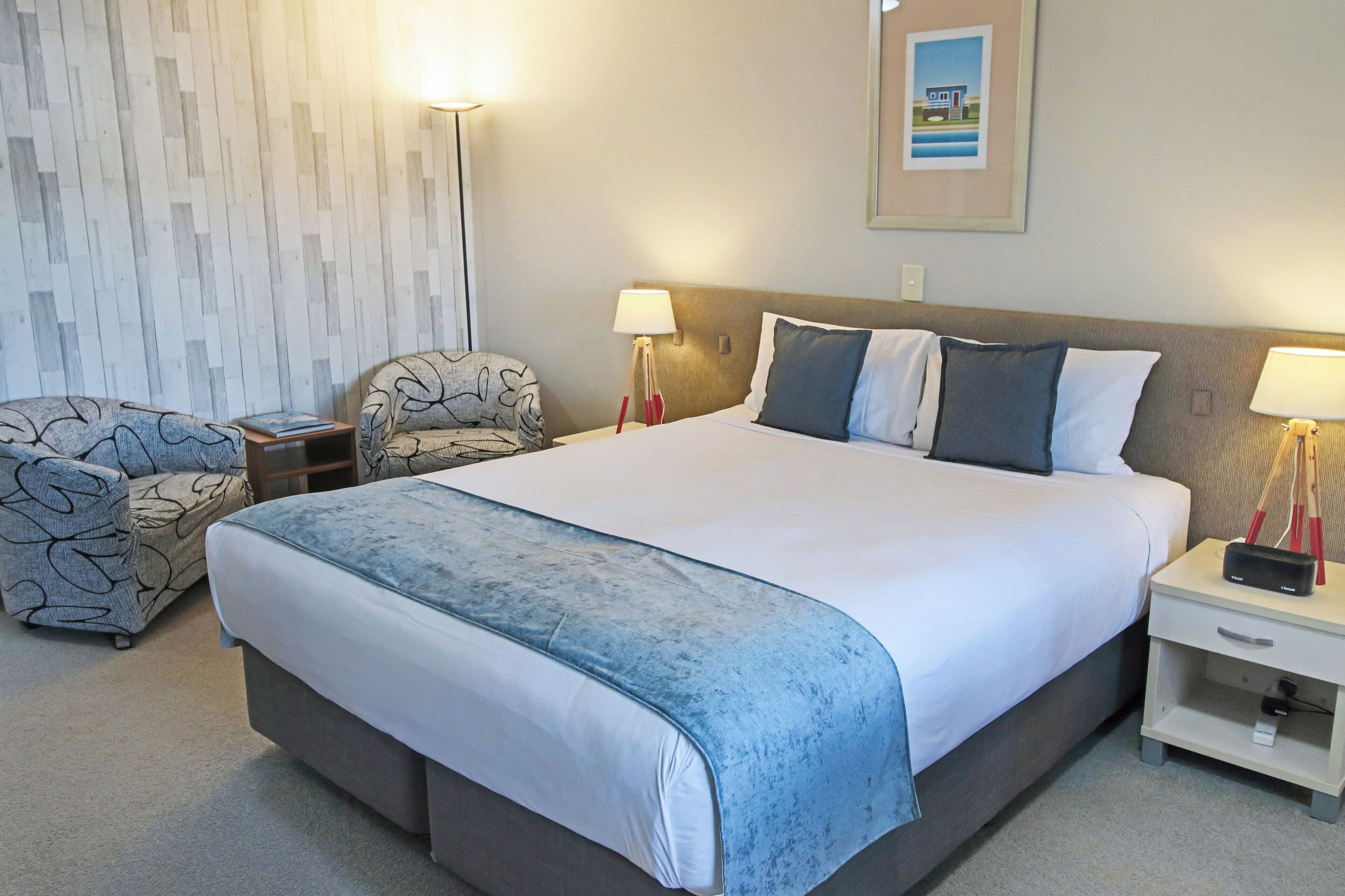 A hotel room with a large bed, two bedside tables, a chair, a lamp, and a framed picture on the wall.