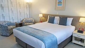 A hotel room with a large bed, two bedside tables, a chair, a lamp, and a framed picture on the wall.