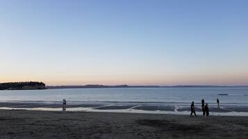 A beach with people walking along the shore, a distant island, and calm waters.