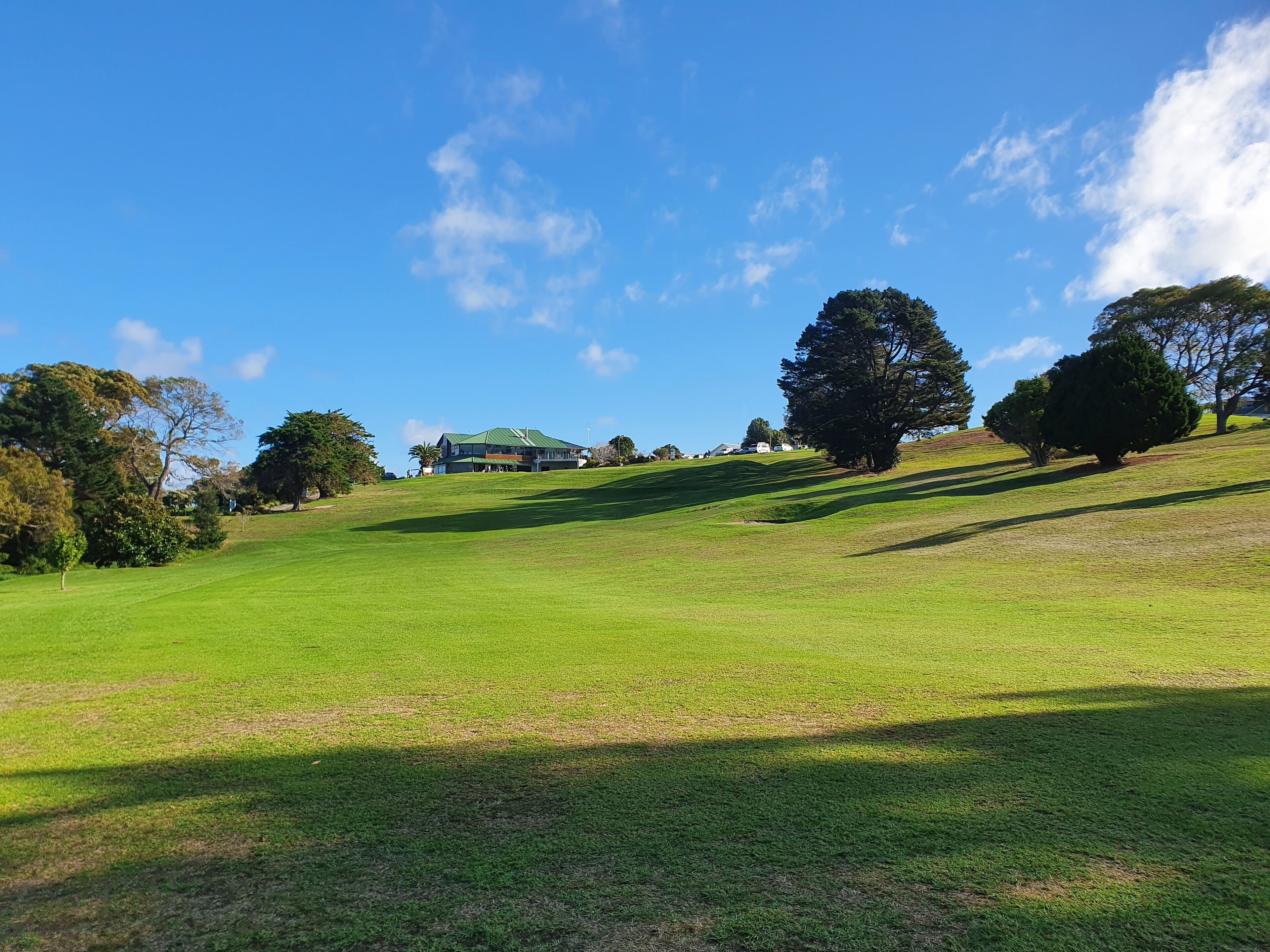 A grassy hill with a building with a green roof in the background.