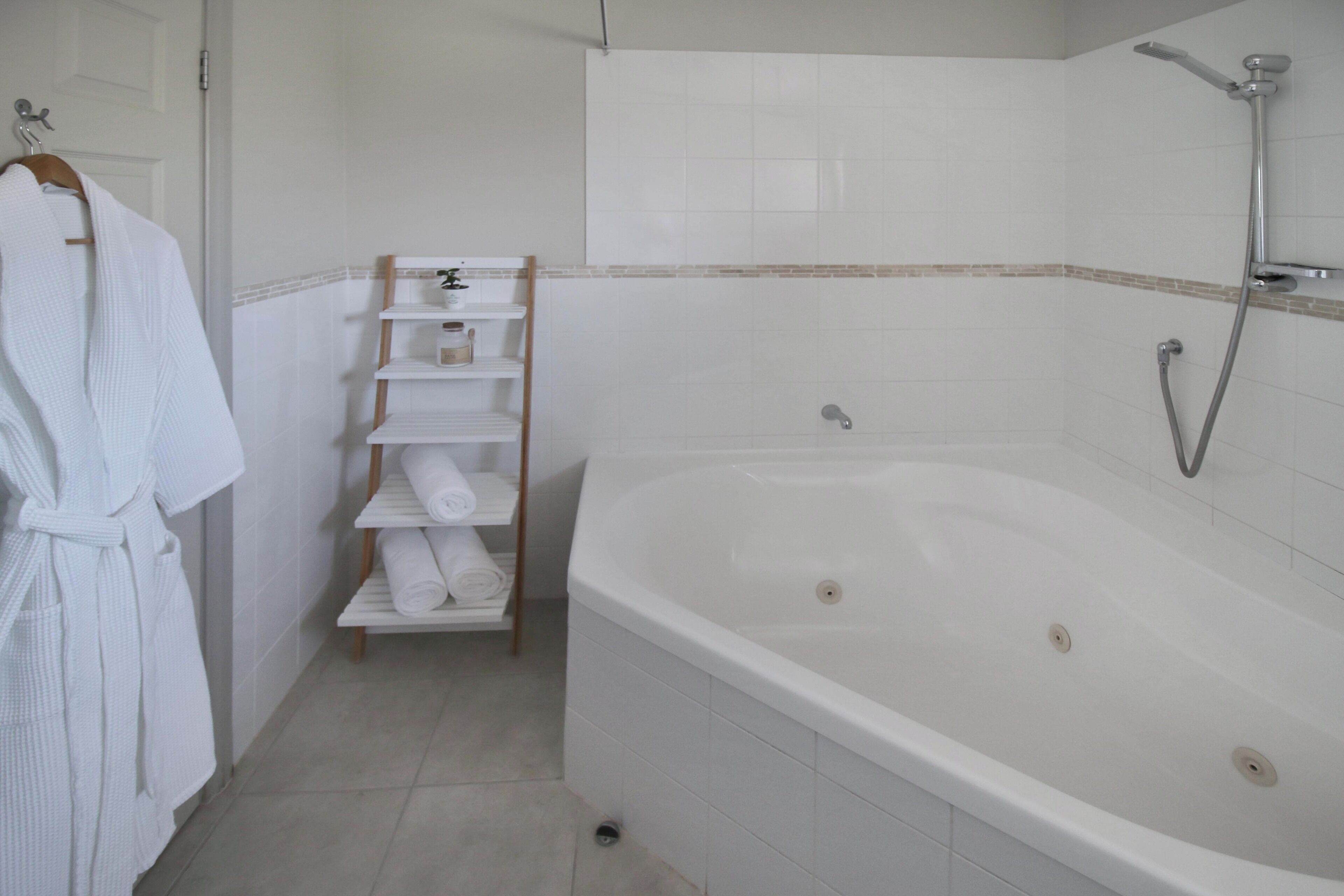 A bathroom with a white bathtub, a wooden towel rack, and a shelf with folded towels.