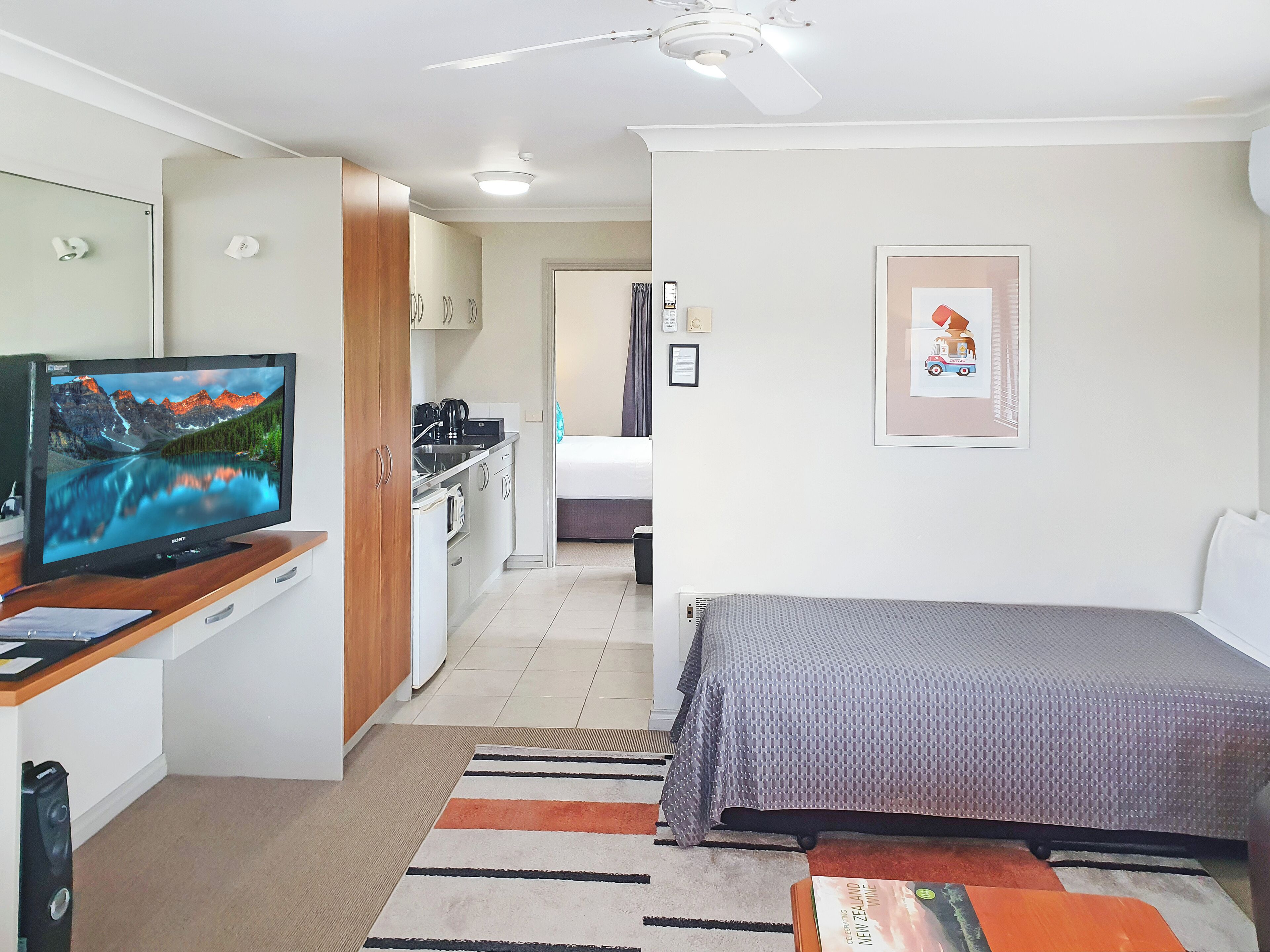 Ein kleines Hotelzimmer mit Bett, Fernseher, Küchenzeile und Badezimmer.