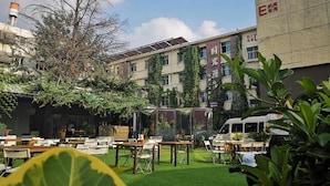 Un espacio al aire libre con mesas y sillas, un edificio con un letrero y un árbol.