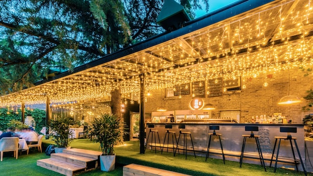Un área de bar al aire libre con césped artificial, escalones de madera y taburetes de bar.