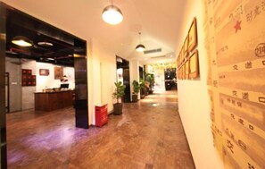 A hotel lobby with a reception desk, potted plants, and a wall with framed pictures. - Nostalgia Hotel（Beijing Yonghe Lama Temple） (Beijing)