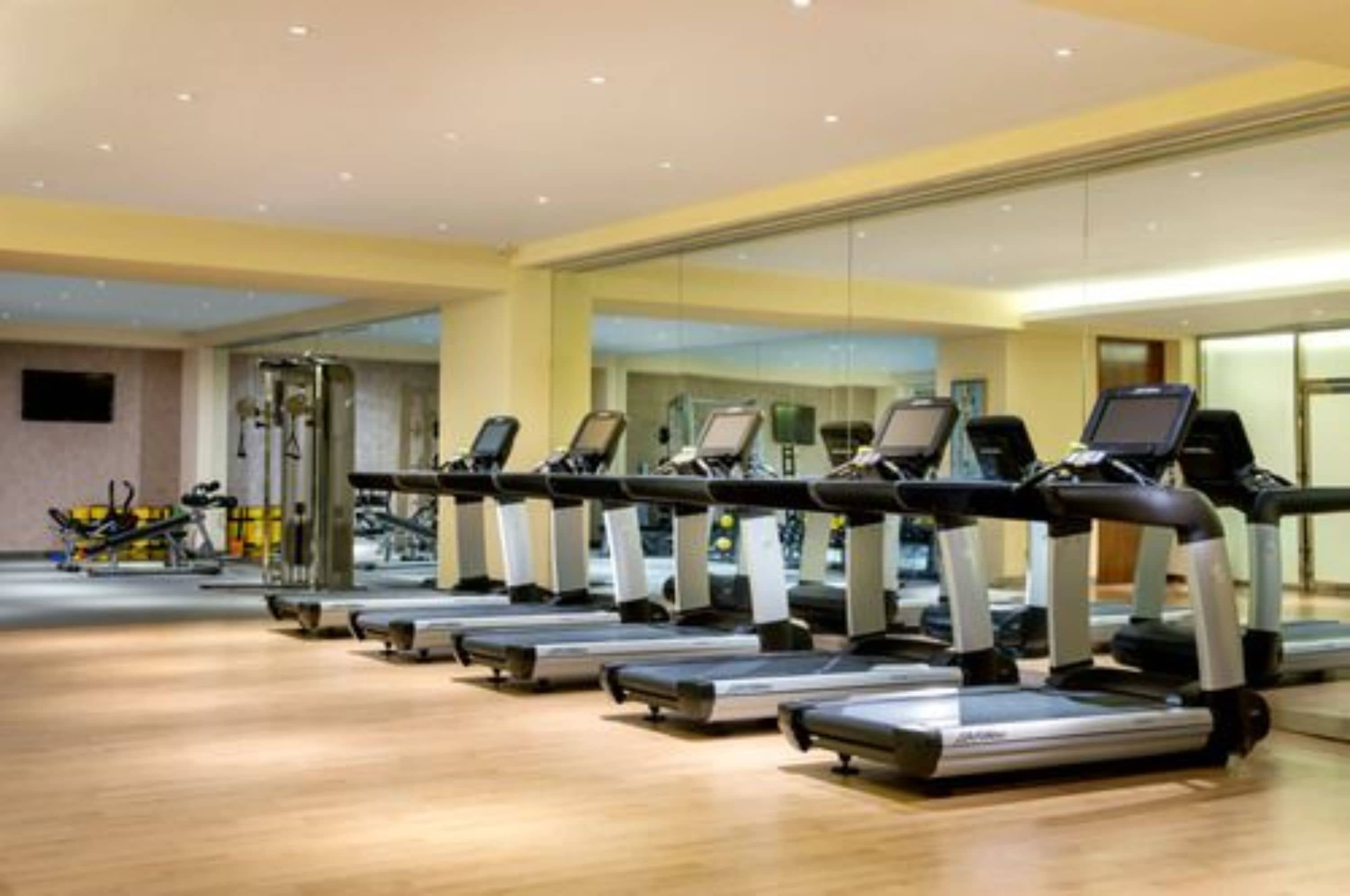 Un gimnasio con cintas de correr, bicicletas estáticas y un espejo grande.