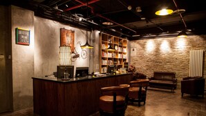 Una zona de bar con mostrador de madera, sillas de cuero, estantería y pared de piedra.