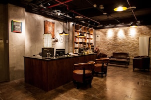 A bar area with a wooden counter, leather chairs, a bookshelf, and a stone wall.
