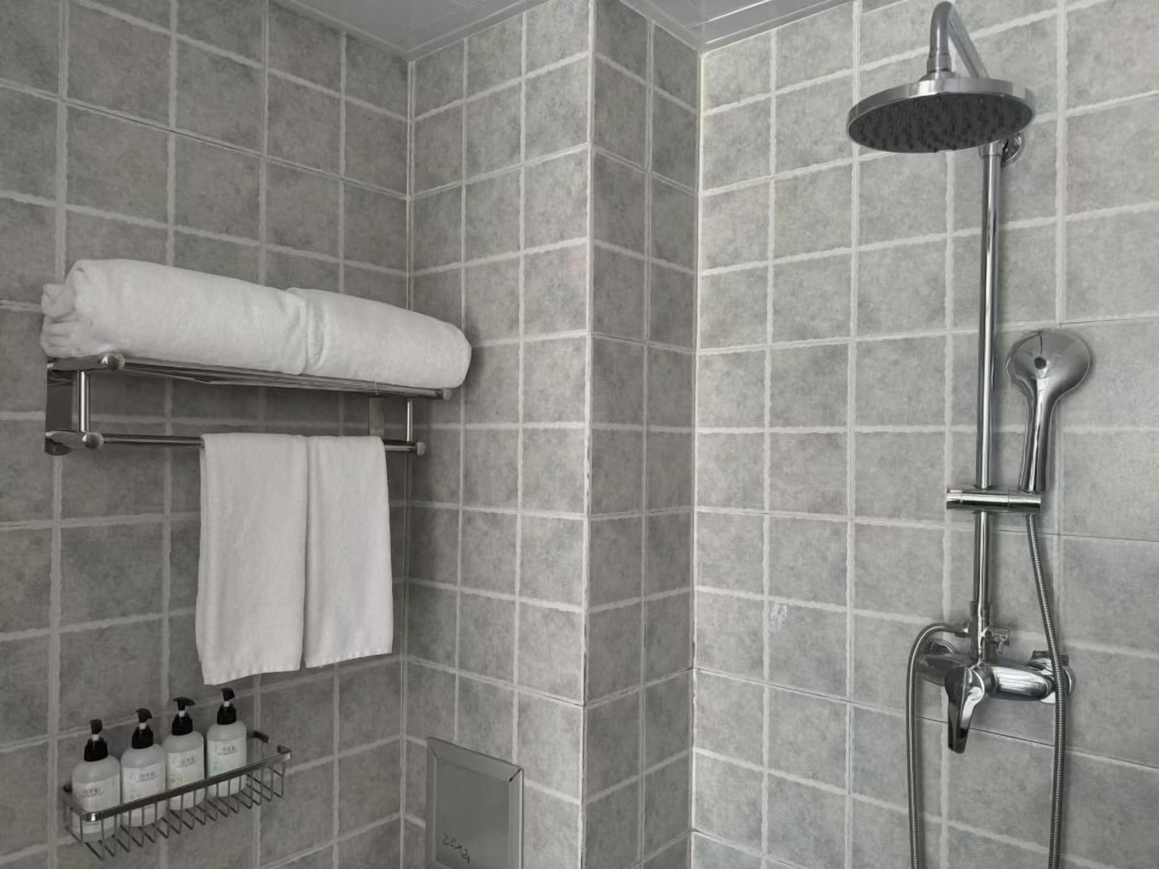Un baño moderno con ducha, un perchero con toallas y un estante con artículos de aseo.