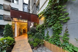 A narrow alleyway with a wooden walkway leading to a building entrance. There are potted plants and a wooden fence along the path.