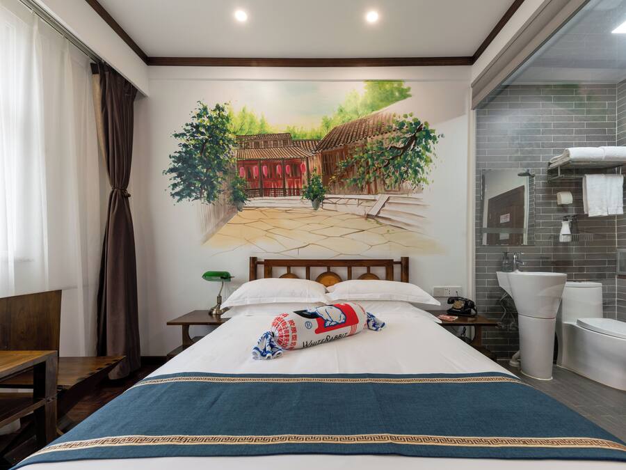 Une chambre d’hôtel comprenant un lit, une table de chevet, un bureau, une chaise et une salle de bain avec des toilettes, un lavabo et un miroir.