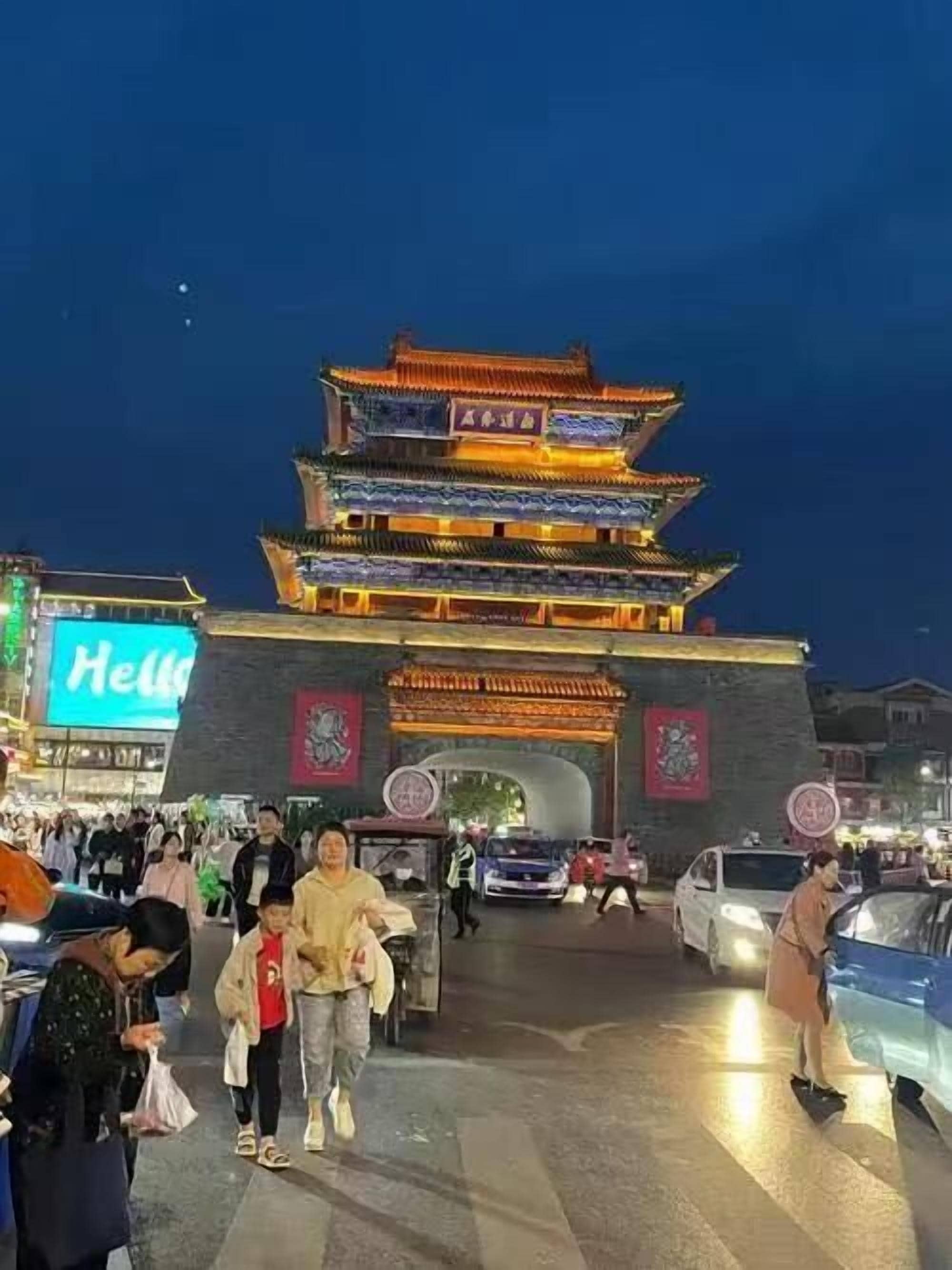 A traditional multi-tiered gate with illuminated details, surrounded by a busy urban environment.