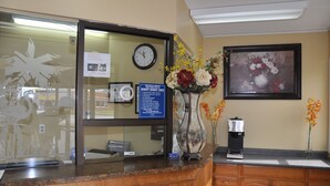 Una reception con una scrivania, un orologio, una targa incorniciata, un vaso con fiori e una macchina per caffè.