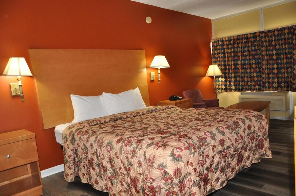Una habitación de hotel con una cama grande, dos lámparas de noche, una silla, un escritorio y una cortina estampada.