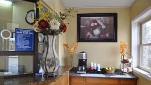 Un'area reception con una macchina per caffè, composizioni floreali e un quadro appeso al muro.
