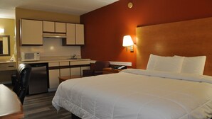 Una camera d'albergo con un letto, una scrivania, una sedia, un forno a microonde, un frigorifero e un angolo cottura.