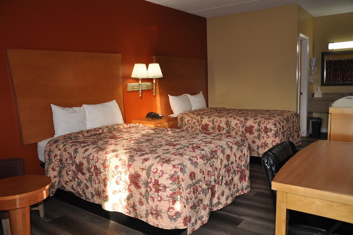 A hotel room with two beds, a wooden table, a small round table, and a nightstand with a lamp.