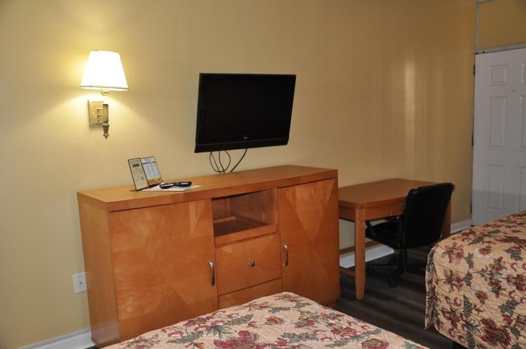 A room with a bed, a desk, a chair, a television, and a lamp.