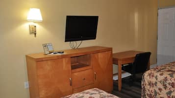 A room with a bed, a desk, a chair, a television, and a lamp.