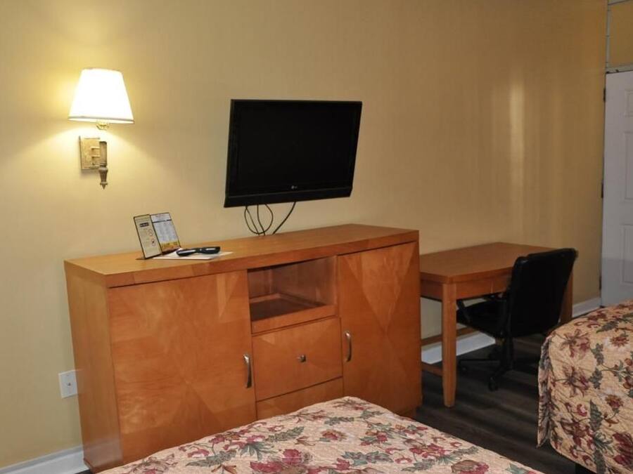 A room with a bed, a desk, a chair, a television, and a lamp.