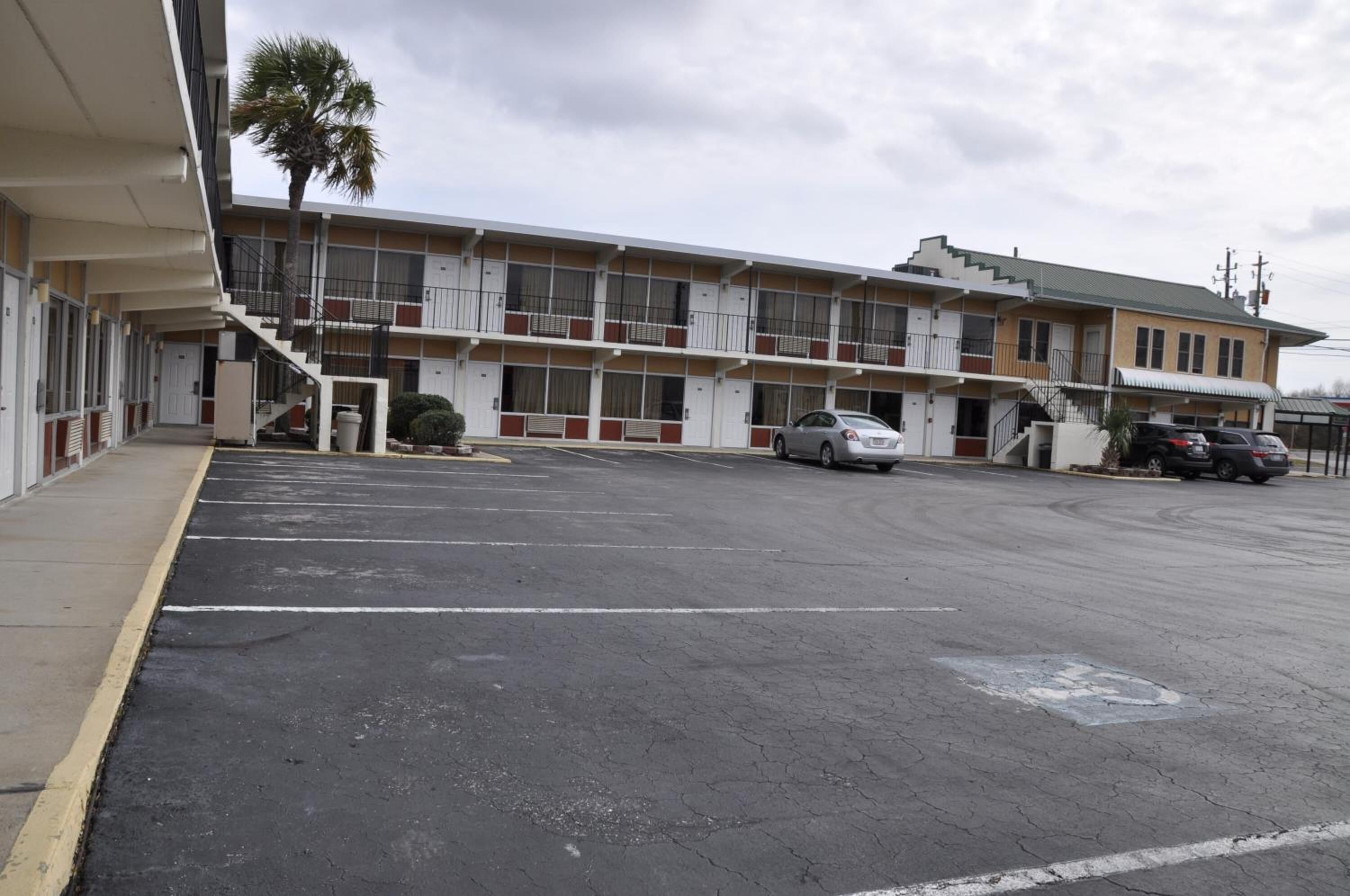 Un motel doté d’un parking, d’un escalier menant à l’entrée et d’un palmier.