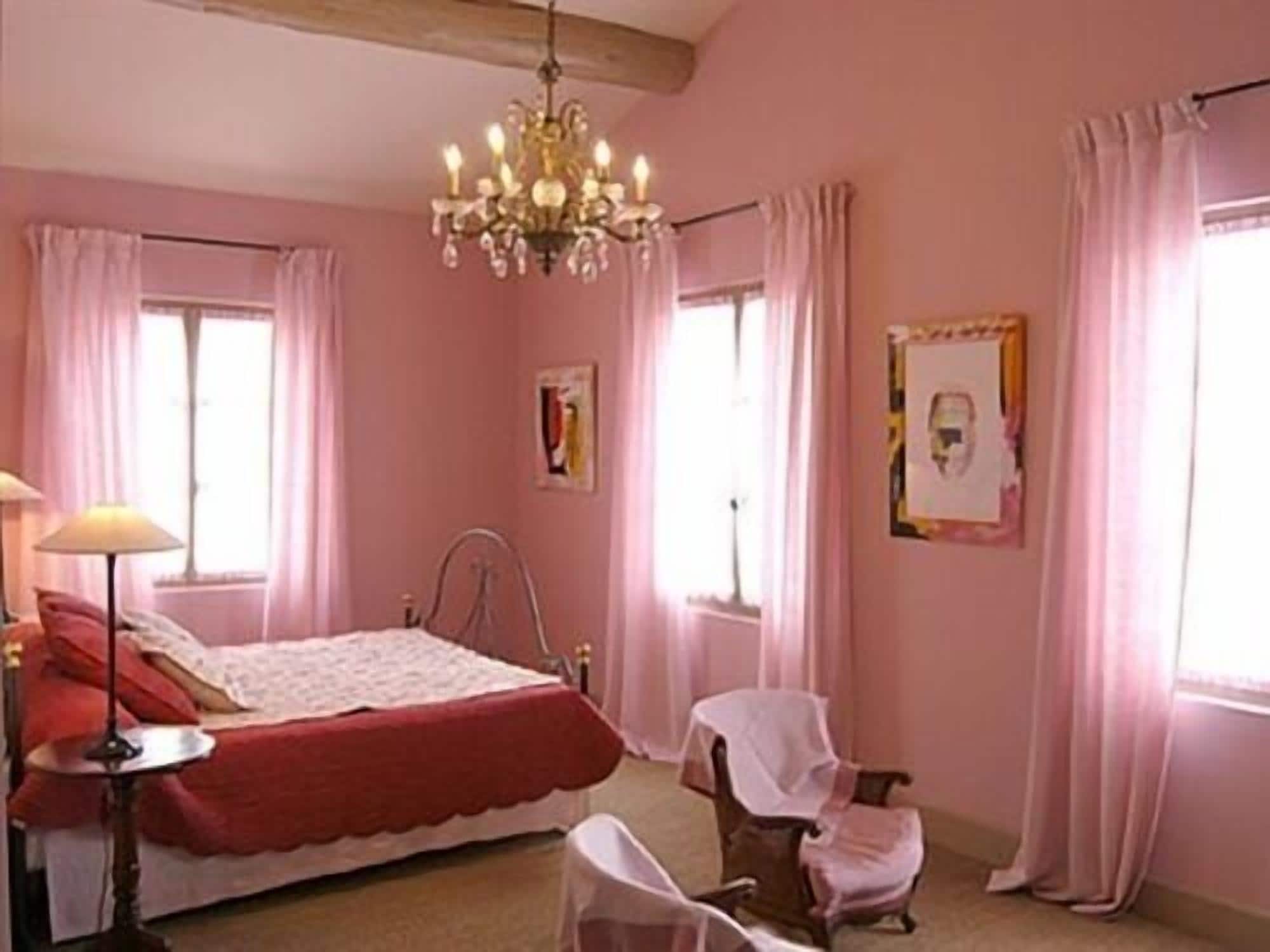 A pink-themed bedroom with a bed, a chair, a lamp, and a chandelier.