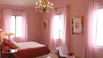A pink-themed bedroom with a bed, a chair, a lamp, and a chandelier.