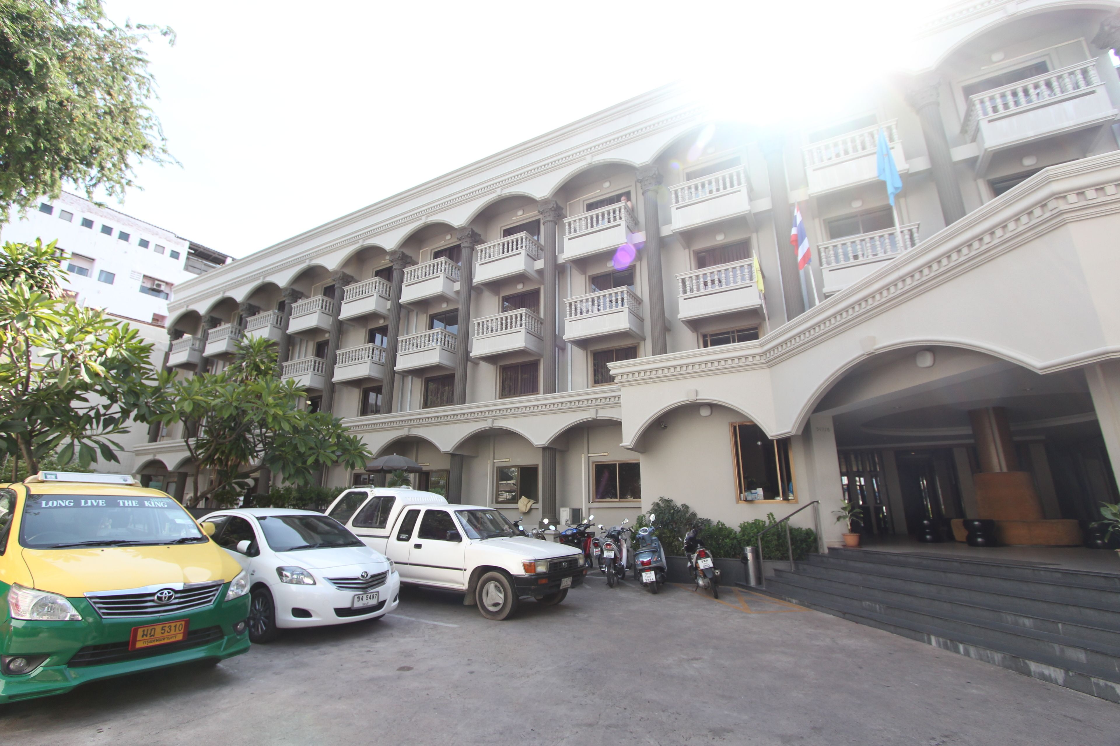 A multi-story hotel with a central courtyard, featuring a white car and a yellow taxi in the parking area.