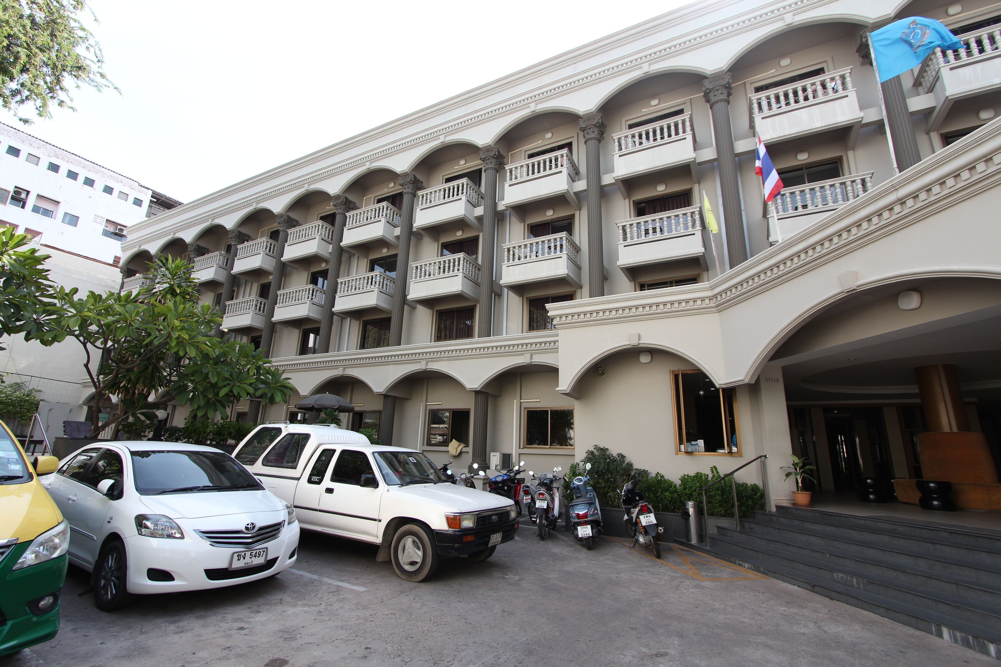 A hotel with multiple balconies, a staircase leading to the entrance, and several parked vehicles.