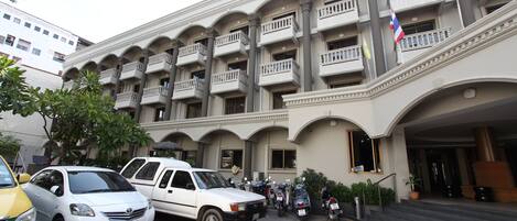 A hotel with multiple balconies, a staircase leading to the entrance, and several parked vehicles.