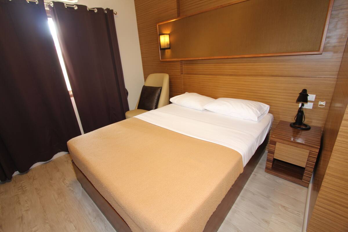 A hotel room with a bed, a chair, a nightstand, and a wall-mounted lamp.