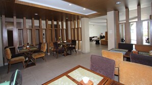 A modern hotel lobby with wooden paneling, a dining area with tables and chairs, and a seating area with cushioned chairs. - Honey Lodge (Pattaya)