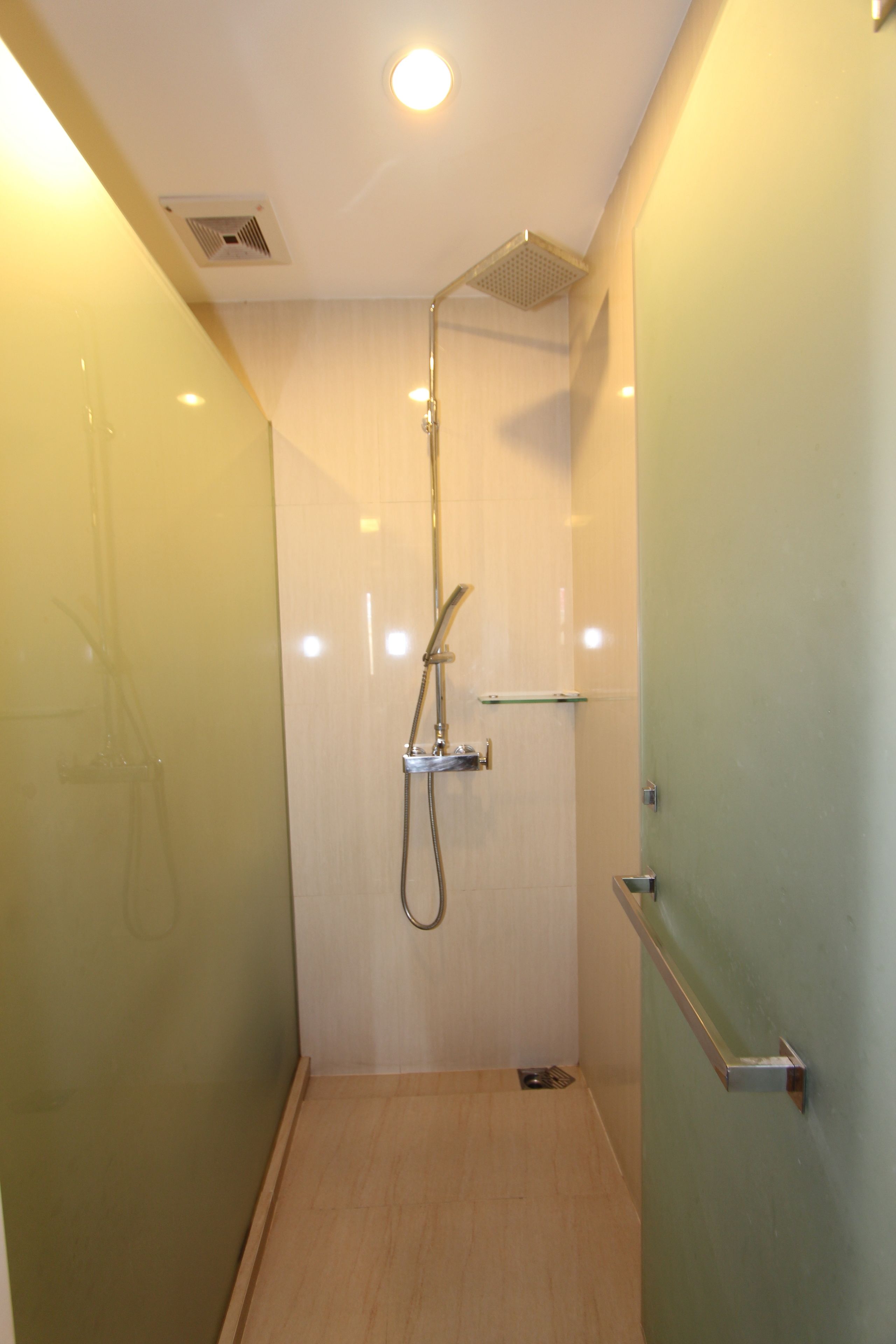 A narrow shower area with a glass door, a showerhead, and a small shelf.