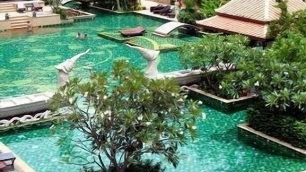 A resort with a large swimming pool surrounded by palm trees and lounge areas. - Villa Thongbura (Pattaya)