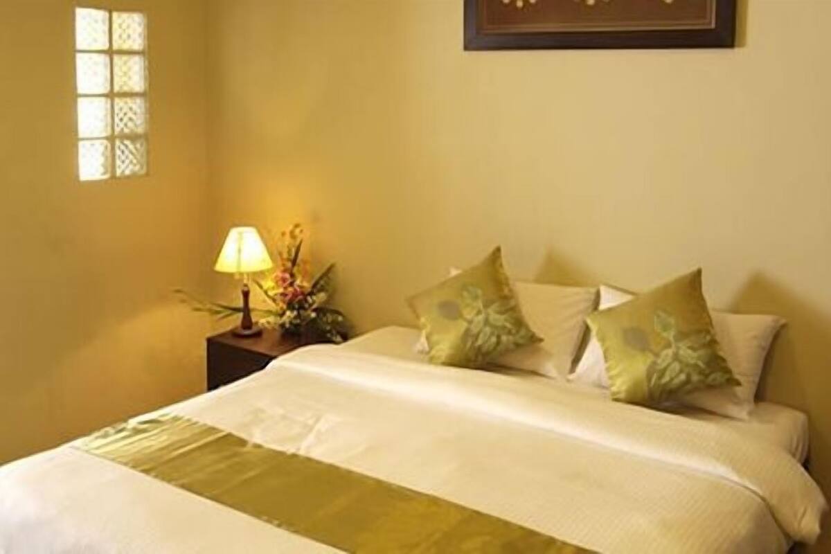 A hotel room with a bed, pillows, a nightstand with a lamp, and a wall-mounted picture.