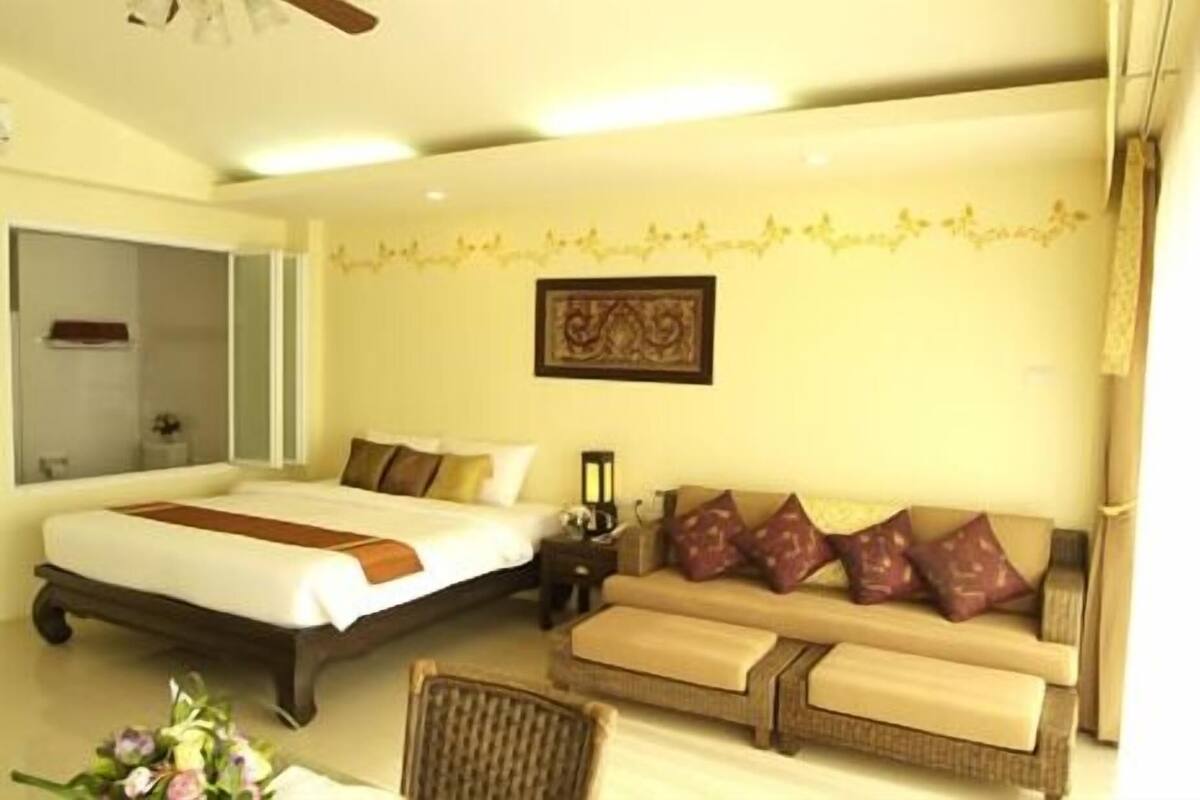 A bedroom with a bed, a sofa, a chair, and a bedside table.