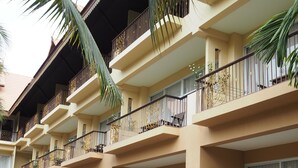A multi-story hotel with balconies, outdoor seating, and palm trees. - Villa Thongbura (Pattaya)