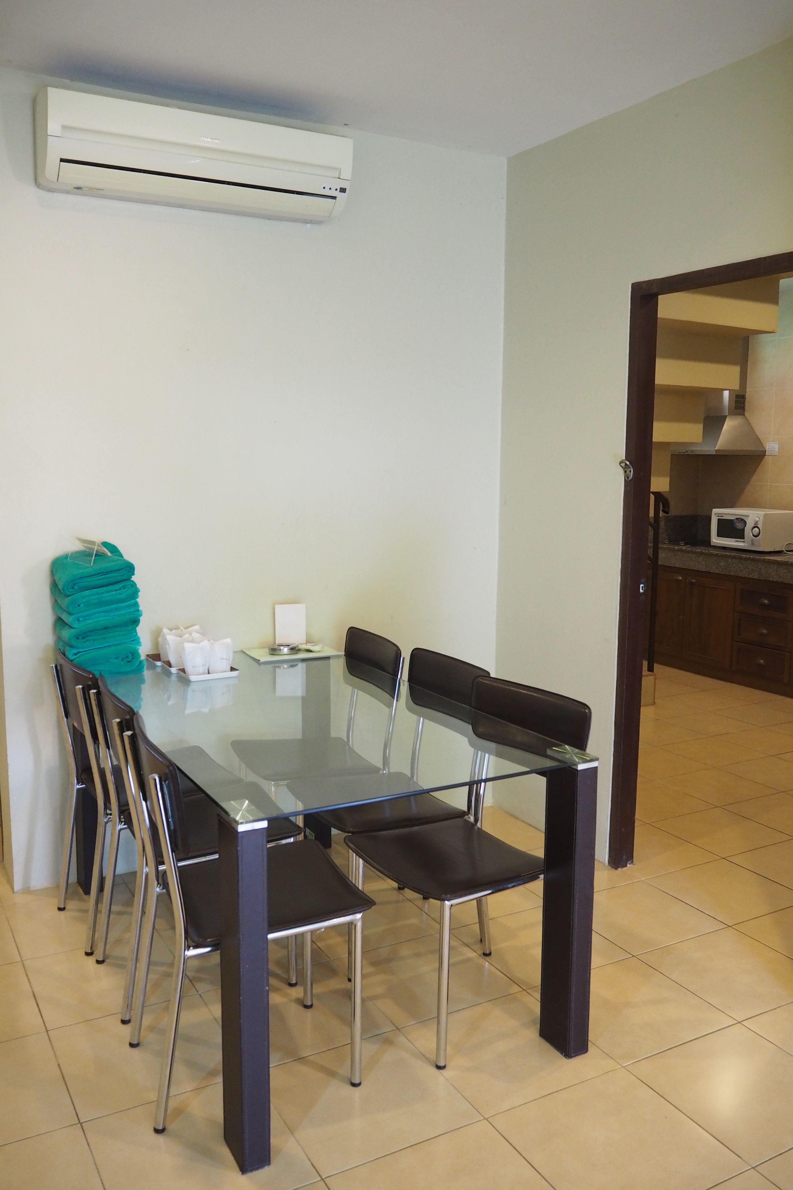Een eethoek met een glazen tafel, zwarte stoelen en een stap opgevouwen handdoeken aan de muur.