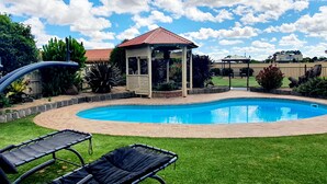 A swimming pool with lounge chairs, a gazebo, and a fenced garden area.