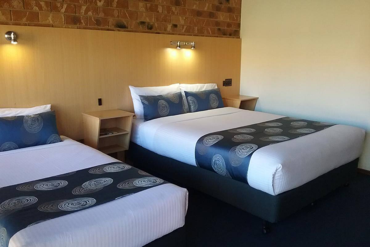 A hotel room with two beds, each with a patterned bedspread and pillows, a wooden headboard, and a nightstand with a lamp.
