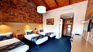 A room with three beds, a wooden ceiling, and a brick wall.
