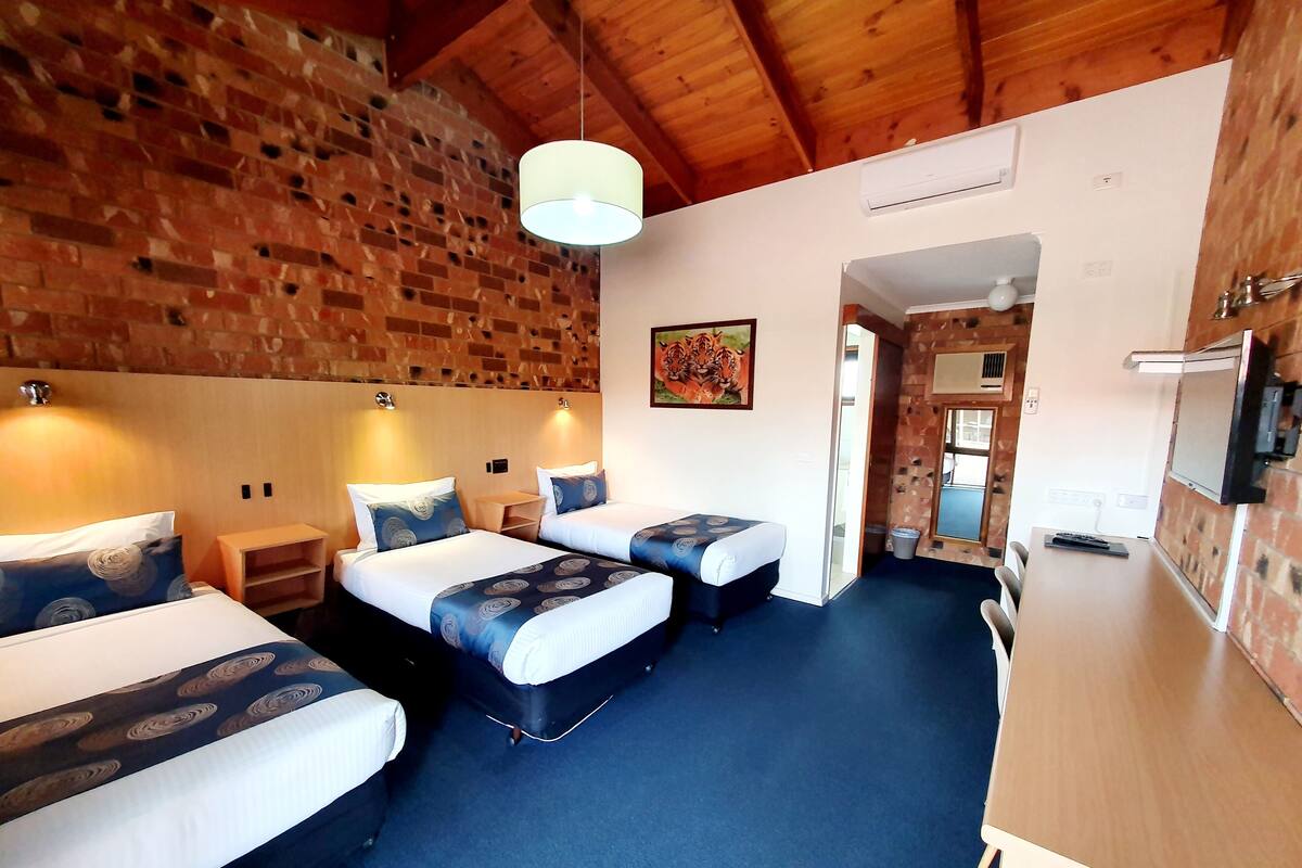 A room with three beds, a wooden ceiling, and a brick wall.