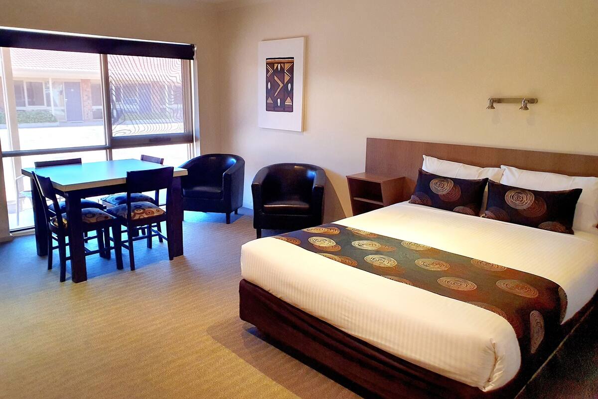 A hotel room with a bed, a desk, two chairs, and a window.