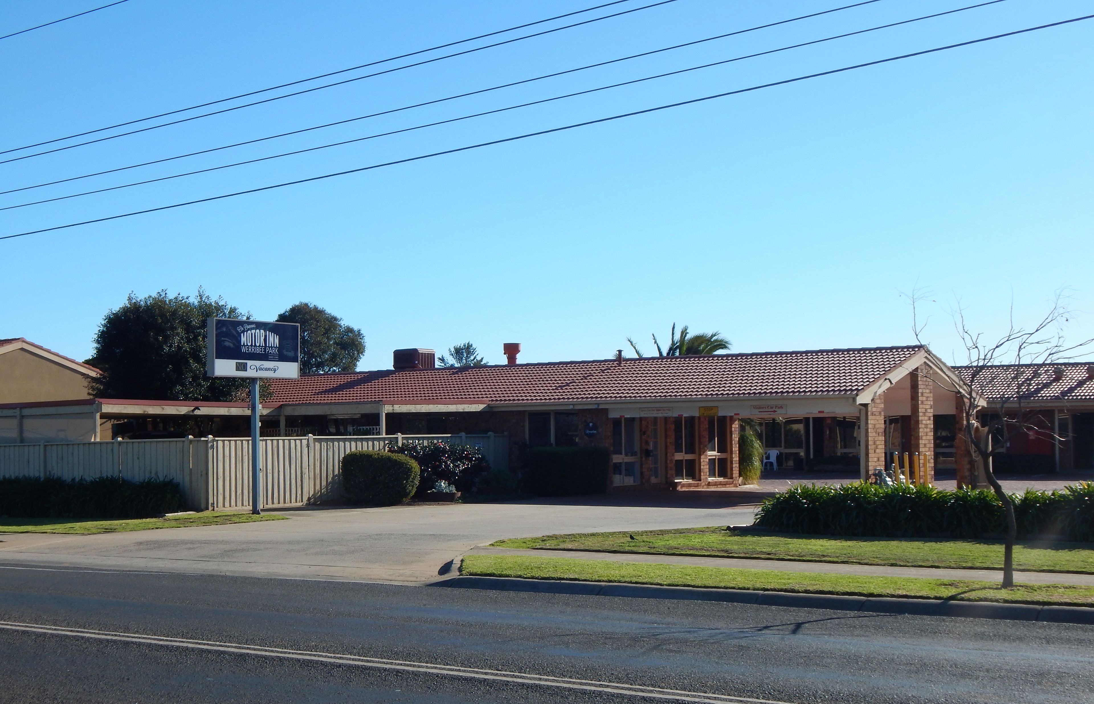 A motel with a red-tiled roof, a covered parking area, and a signboard advertising the motel.