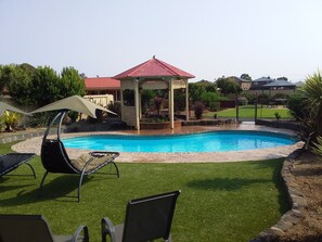 Ein Garten mit Swimmingpool, einem Pavillon und zwei Liegestühlen.