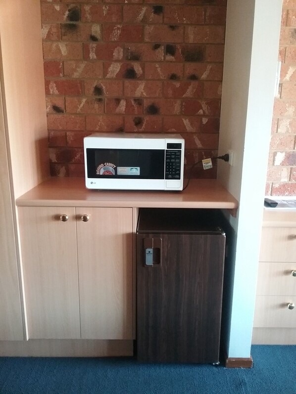 A compact kitchenette with a microwave on a shelf, a small refrigerator, and a wooden cabinet.