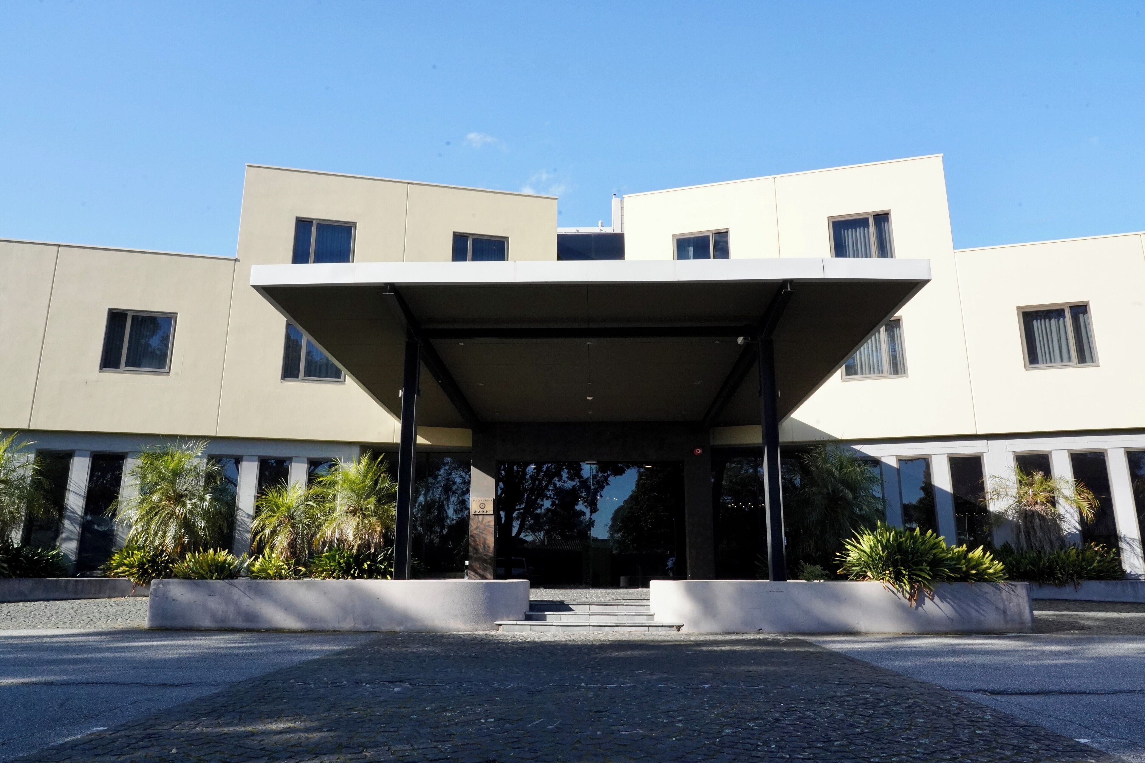 A modern building with a covered entrance, large windows, and landscaped areas with plants.